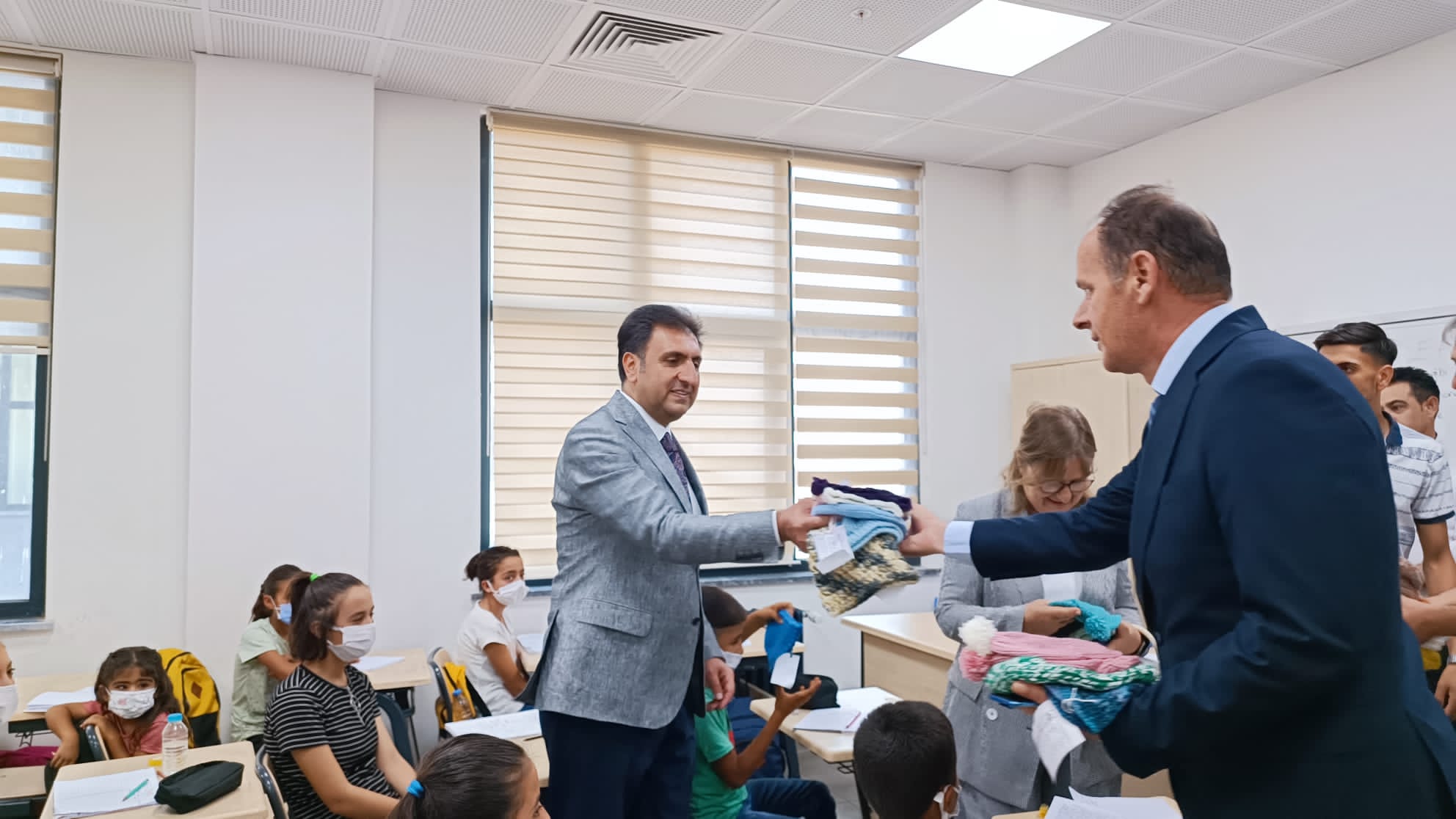 A Woolly Wishes volunteer handing a stack of handmade knitwear to a school staff member in Izmir